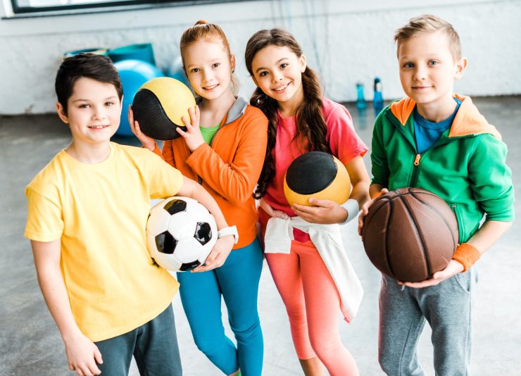 Excited children in sportswear posing with balls